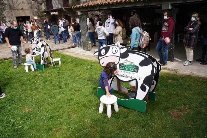 Varias personas compran productos lácteos, mientras unos niños juegan a ordeñar, en el Xanceda Market , en la granja Casa Grande de Xanceda