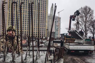 Varios operarios cargan losas de cemento frente a un miliciano ucraniano, a 2 de marzo de 2022, en Kiev (Ucrania)