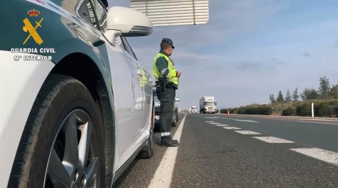 Un agente de la Guardia Civil junto a su coche en una carretera.