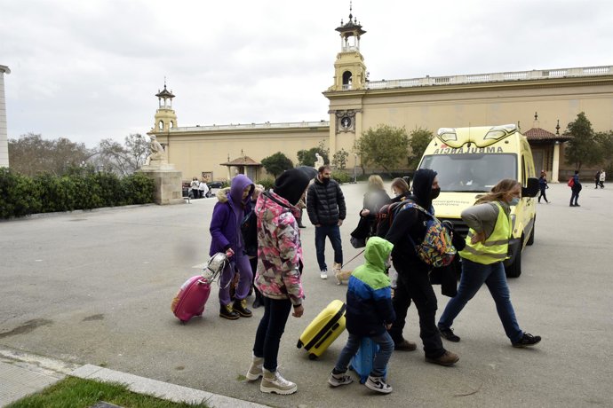Diversos refugiats i una traductora al costat d'una ambulncia a l'entrada del palau de Victria Eugnia