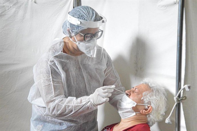 Archivo - Un profesional sanitario practica una prueba de detección del coronavirus a una mujer mayor.