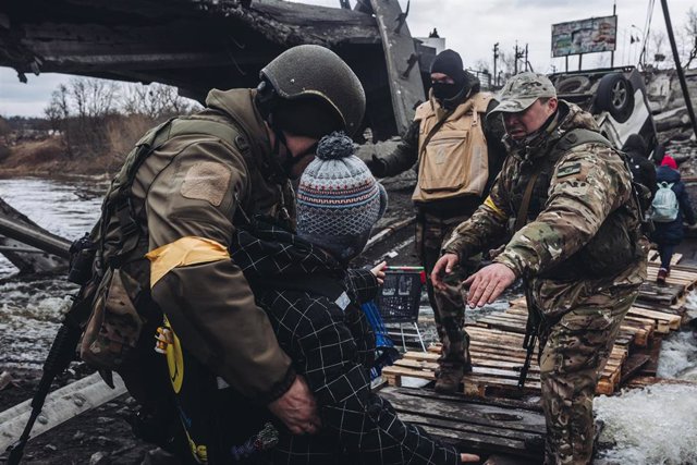 Unos soldados ayudan a cruzar el río a un niño, a 7 de marzo de 2022, en Irpin (Ucrania).