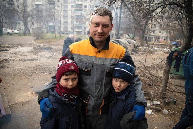 03 April 2022, Ukraine, Mariupol: A wounded man stands with his children in a destroyed neighbourhood in Mariupol during Russia's invasion of Ukraine. By capturing the Ukrainian port city of Mariupol, Russia says it wants to create a secure land link to t