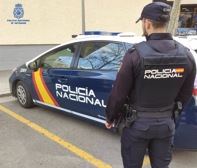 Un agente de la Policía Nacional en Palma junto al coche policial.