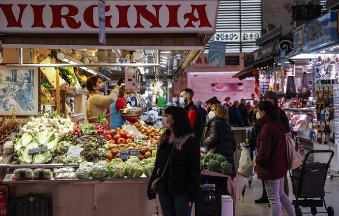 Varias personas compran en un puesto de fruta y verdura en el Mercado Central de Valencia,