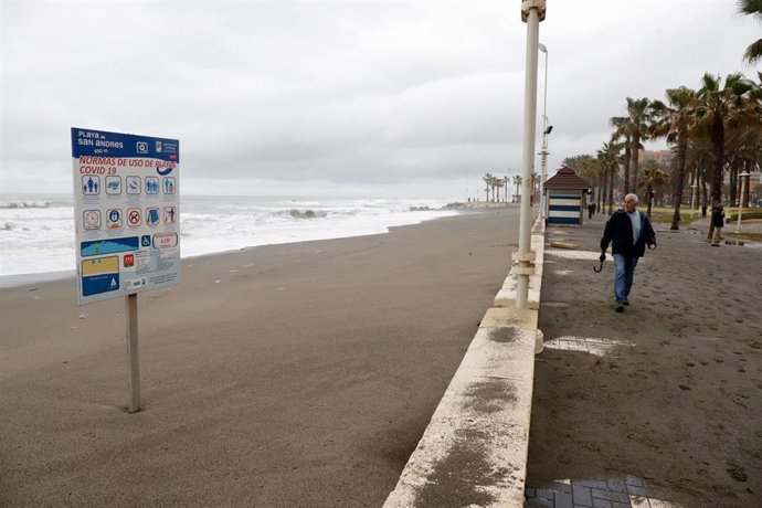Una persona pasea por la playa de Huelín donde los desperfectos causados por el temporal en las últimas horas han dejado los chiringuitos anegados por las inundaciones  
