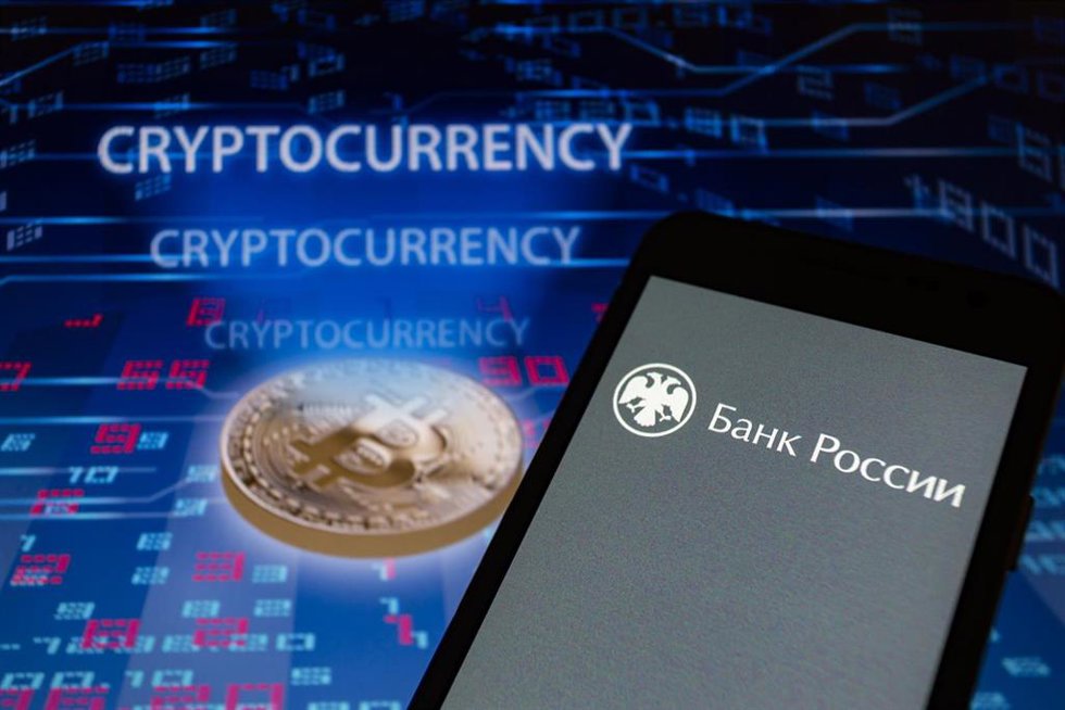 El logotipo ruso del Banco Central de la Federación de Rusia, también conocido como Banco de Rusia, se muestra en un teléfono inteligente con una representación visual de la criptomoneda.
