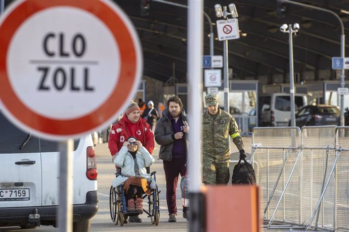 17 March 2022, Slovakia, Vysne Nemecke: A Red Cross helper and an officer of the Slovak police escort a man and a woman in a wheelchair across the border into Slovakia. According to local officials, the flow of refugees is increasing and the city of Uzh
