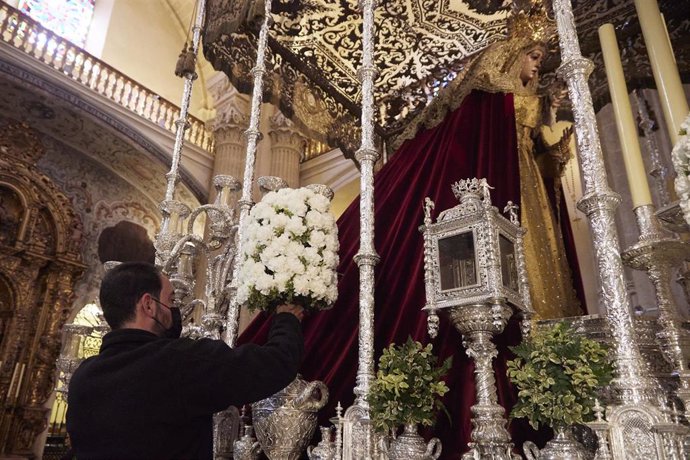 Un florista coloca un ramo de claveles blancos en el palio de la Virgen del Socorro, de la hermandad del Amor.