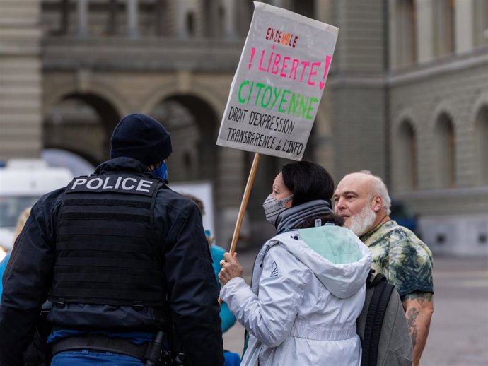 Un manifestante que se opone a las restricciones de Covid-19 se encuentra junto a un agente de policía frente al Palacio Federal, un día después de que el Consejo Federal impusiera medidas nacionales más estrictas