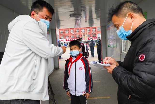 Un profesor mide la temperatura corporal de un alumno en la escuela primaria experimental de la ciudad de Tengzhou. 