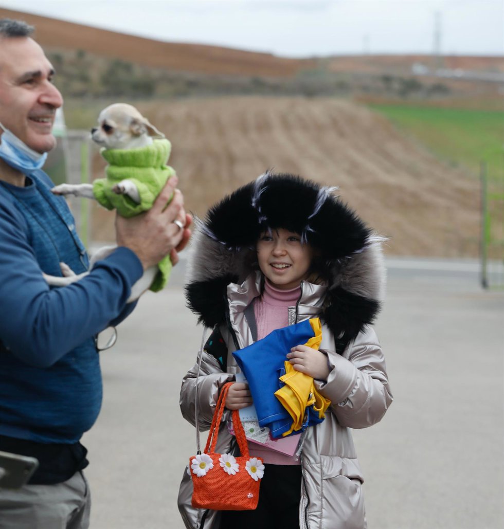 Una niña refugiada, con una bandera de Ucrania, junto a un hombre y su mascota.
