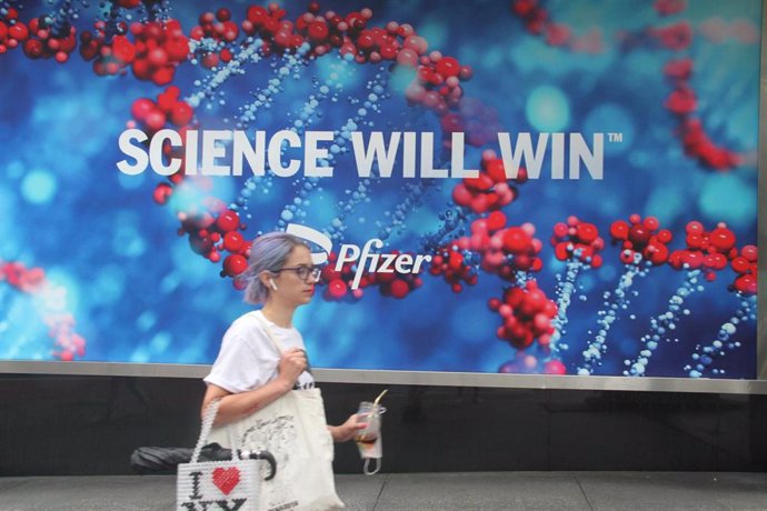 Archivo - Una mujer camina junto a un cartel de la farmacéutica Pfizer, investigadora de una de las vacunas contra la COVID-19