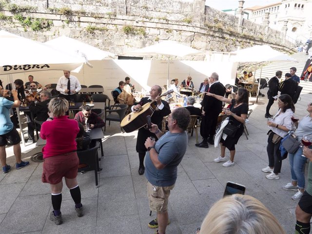 Archivo - Un grupo de turistas canta con una tuna en una plaza de Santiago de Compostela.