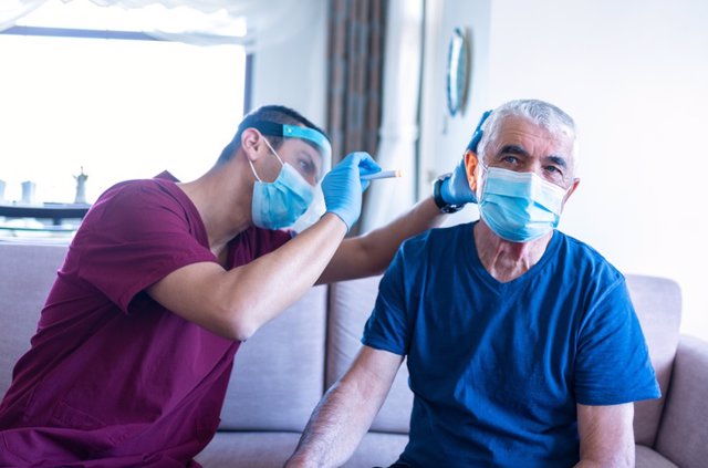 Archivo - El trabajador sanitario masculino examina el oído del anciano en su casa durante la epidemia de coronavirus.