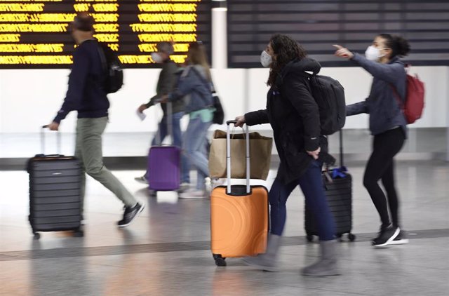 Varias personas, con maletas, pasan junto a un panel de salidas con diferentes destinos, en la estación Madrid - Puerta de Atocha