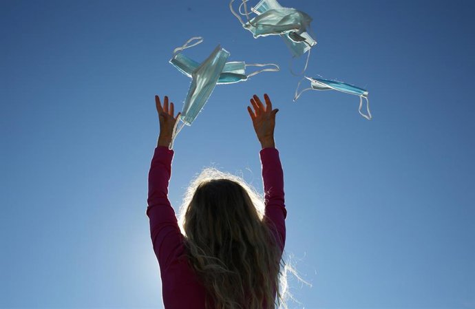 Archivo - Una mujer tira mascarillas al aire