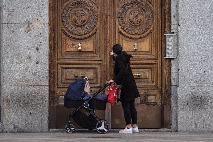 Archivo - Una mujer frente a un portal de la capital con un carrito de bebé