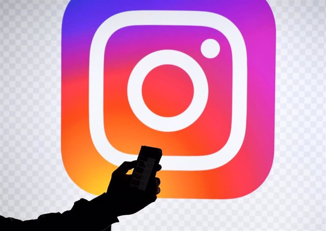 Archivo - Un hombre sostiene un teléfono ante el logo de Instagram. 