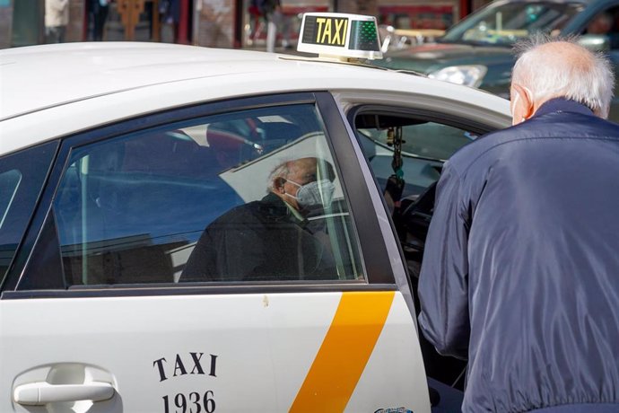 Una persona mayor con mascarillas coge un taxi el día