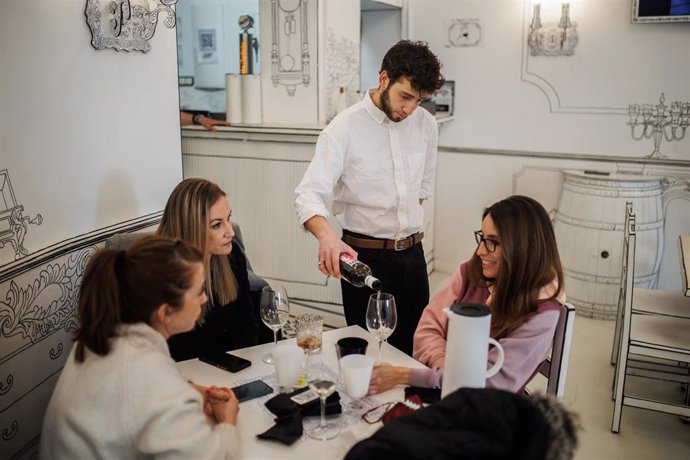 Un camarero sirve una copa de vino a varias mujeres el día en que ha entrado en vigor el decreto que pone fin al uso de la mascarilla en la mayoría de interiores, en el restaurante Estando contigo', a 20 de abril de 2022, en Madrid (España). Desde hoy,