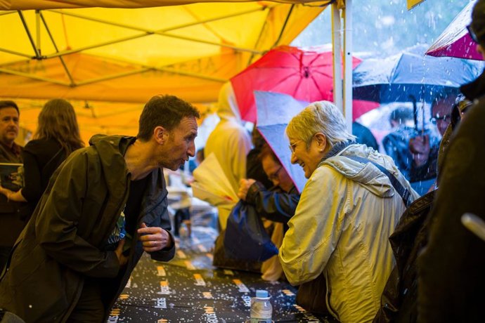 El periodista Manel Alías protegit de la pluja durant el dia de Sant Jordi, en una parada de llibres