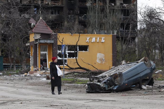 MARIUPOL, April 22, 2022  -- A woman walks past a damaged car in the port city of Mariupol, April 21, 2022. Russian President Vladimir Putin on Thursday ordered a blockade of the Azovstal plant in the port city of Mariupol instead of storming it, local 