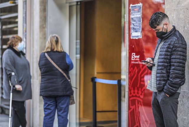 Archivo - Un joven mira su teléfono móvil mientras espera para entrar en una oficina del SEPE