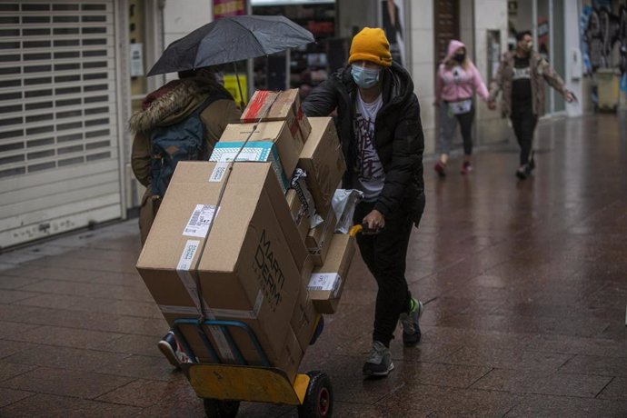 Archivo - Un repartidor lleva unas cajas durante una llovizna en una imagen de archivo.