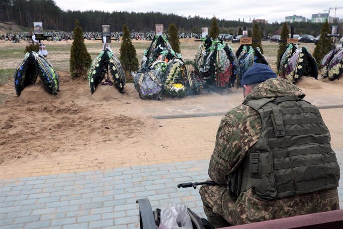 April 20, 2022, Irpin, Kyiv Region, Ukraine: An armed soldier in a camouflage uniform and bulletproof vest faces the graves of those who perished in the war at the central cemetery of Irpin, a city liberated from Russian invaders, Kyiv Region, northern 