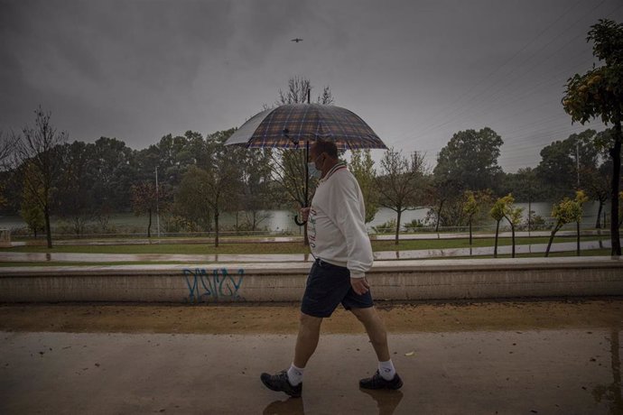 Archivo - Un hombre camina protegido de la lluvia con un paraguas.