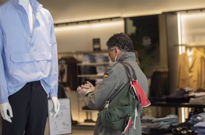 Archivo - Un hombre se desinfecta unos guantes proporcionados en la entrada de una tienda de ropa