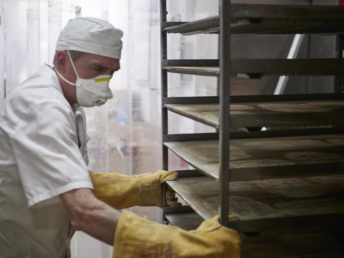 Archivo - Un trabajador protegido con mascarilla maneja bandejas para cocer pan en una imagen de archivo.