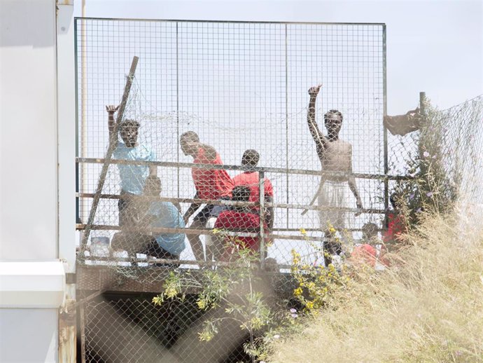 Archivo - Varios migrantes detrás de una valla en la Ciudad del Fútbol del Altos del Real