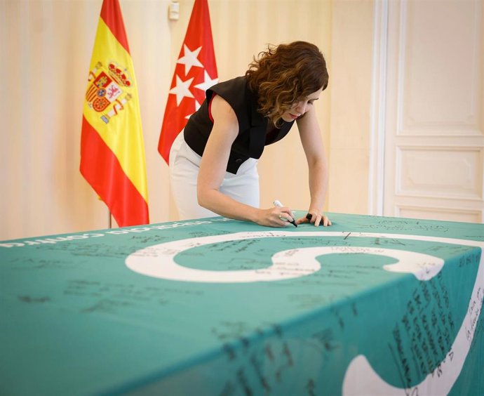 La presidenta de la Comunidad de Madrid, Isabel Díaz Ayuso, firma la bandera de la AECC