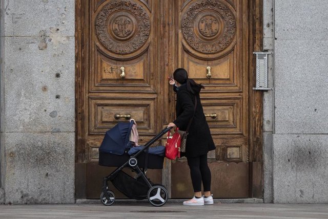 Archivo - Una mujer frente a un portal de la capital con un carrito de bebé, a 30 de marzo de 2020.