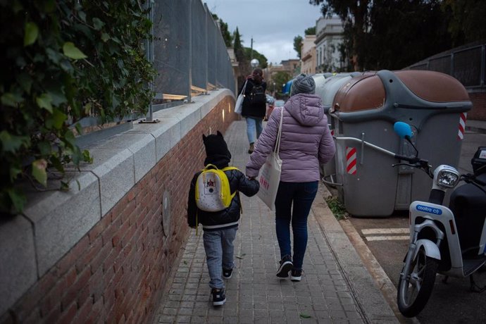 Archivo - Una mujer lleva de la mano a un niño a clase