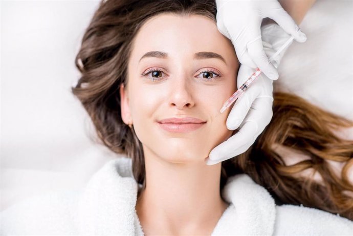 Woman receiving a botox injection in the lips zone lying on the medical couch