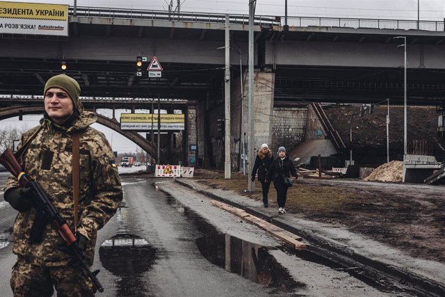 Archivo - Dos mujeres caminan frente a un miliciano ucraniano, a 2 de marzo de 2022, en Kiev (Ucrania). Las autoridades de Kiev han declarado el toque de queda en la ciudad ante la situación causada por la ofensiva rusa en el país. Más de 2.000 civiles uc