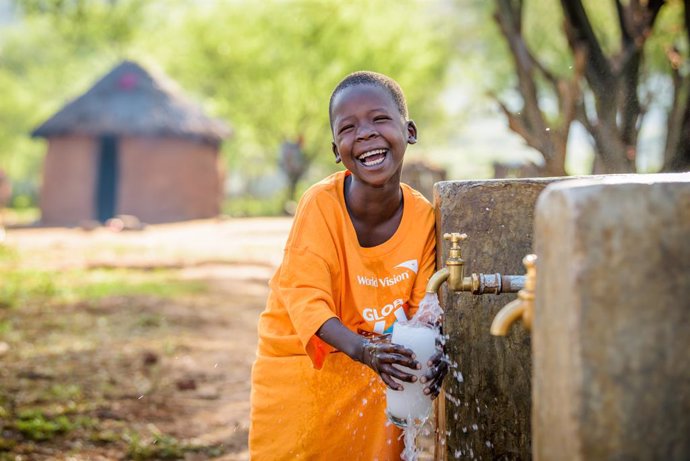 Happy Cheru, wearing a World Vision Global 6K t-shirt, fills her glass at the water point at her home, and takes a drink of clean water.  Cheru, 6, benefits from a 16 km gravity-fed World Vision pipeline that brings clean water to her community.