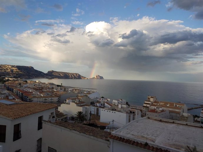 Archivo - El casco urbano de Altea y al fondo, bajo una tormenta y un arcoiris, el Penyal d'Ifach en Calp.