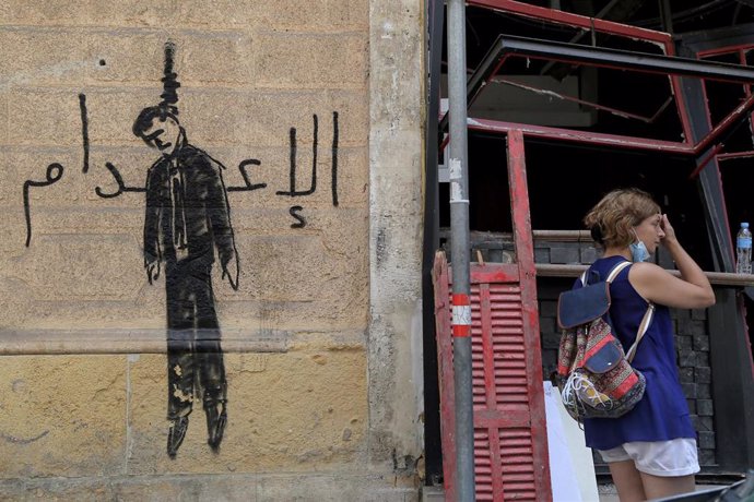 Archivo - Una mujer junto a un grafiti en el que se puede ver una figura ahorcada y la palabra "ejecución" en una pared en la capital de Líbano, Beirut