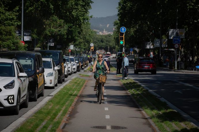 Una mujer pasa montada en bicicleta en una marcha lenta de taxistas contra los VTC, a 18 de mayo de 2022, en Barcelona, Catalunya (España). El sector del taxi vuelve a salir a las calles de Barcelona para protestar contra los VTC y exigir que se siga ma