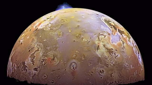 Imagen tomada por la misión Galileo de la NASA del terreno accidentado y las erupciones volcánicas de Io (explosión azul en la parte superior de la imagen).