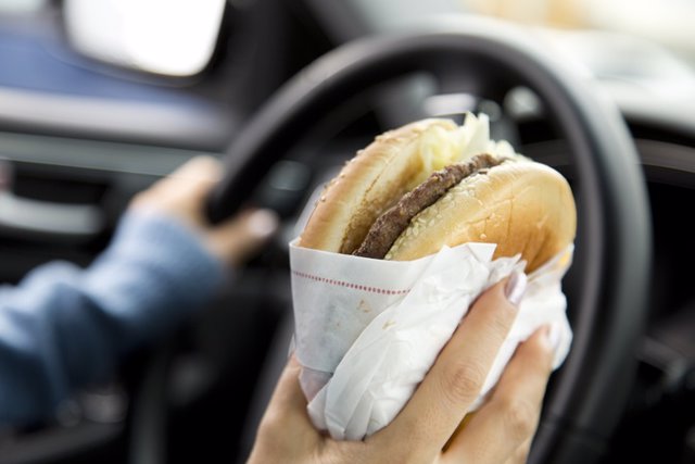 Archivo - Hombre al volante comiendo una hamburguesa.