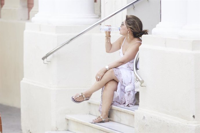 Una señora bebe agua mientras descansa sentada en una escalera durante el primer día de altas temperaturas en Sevilla, a 19 de mayo de 2022 en Sevilla (Andalucía, España)