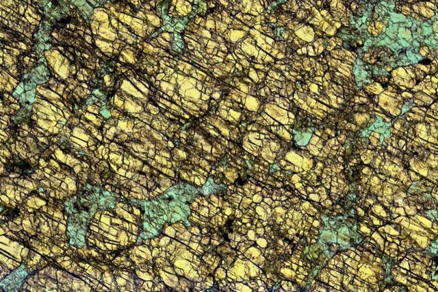 Fotografía microscópica de una roca de la corteza del arco inferior utilizada en el estudio que muestra minerales de granate (rojo) y clinopiroxeno (verde).