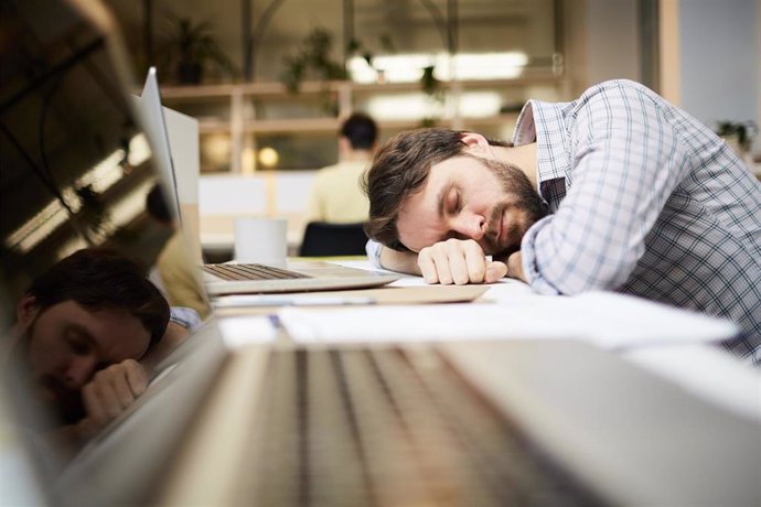 Hombre duerme junto a un ordenador portátil.