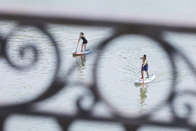 Dos personas practican padel surf bajo el puente de Isabel II durante el primer día de altas temperaturas en Sevilla, a 19 de mayo de 2022 en Sevilla (Andalucía, España)