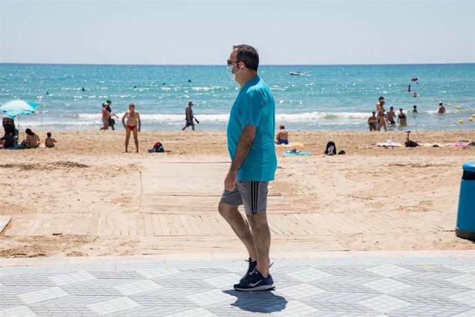 Archivo - Un hombre protegido con mascarilla pasea por el paseo marítimo junto a la Playa del Postiguet